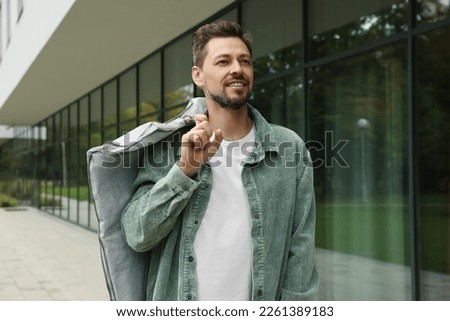 Attractive happy man holding garment cover with clothes outdoors. Dry cleaning service Royalty-Free Stock Photo #2261389183