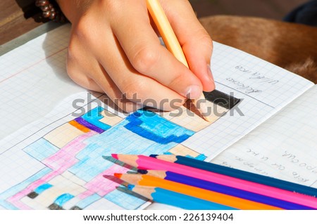 Child hand draws the multicolored minecraft picture. Outdoors close-up.
