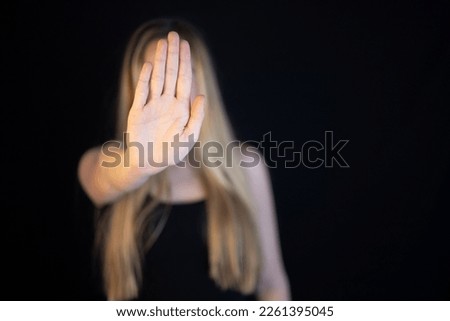 Woman showing hand stop sign to campaign against gender violence and pain. Hand raised to dissuade for self harm awareness, stop abusing and bullying. Human rights. Black background with copy space. 