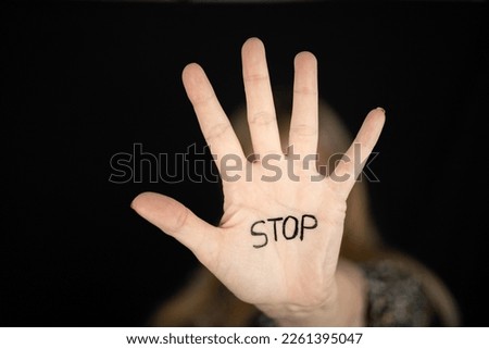 Woman showing hand stop sign with word STOP written to campaign against gender violence and pain. Hand raised to dissuade for self harm awareness, stop abusing, bullying, mental health. Copy space.