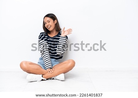Young caucasian woman sitting on the floor isolated on white background saluting with hand with happy expression