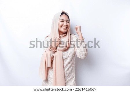 A young Asian Muslim woman with a happy successful expression wearing a hijab isolated by white background Royalty-Free Stock Photo #2261416069