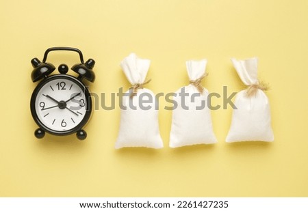 Flatlay picture of alarm clock with fake money bag on yellow background. Profit in business concept.