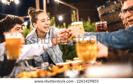Happy friends clinking and toasting beer at brewery restaurant patio - Life style and beverage concept with young people having fun together out side at patio garden by night - Warm evening filter Royalty-Free Stock Photo #2261429855