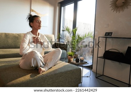 Woman meditating at home with eyes closed  Royalty-Free Stock Photo #2261442429