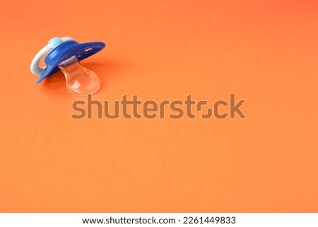 One blue baby pacifier on orange background. Space for text