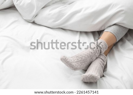 Woman wearing warm socks in comfortable bed, closeup. Space for text Royalty-Free Stock Photo #2261457141