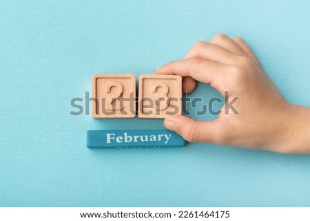 Hand holding calendar february date 23 on a blue background.