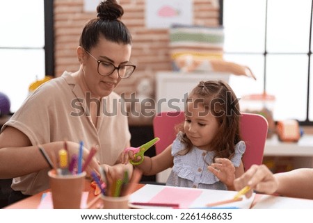Teacher and toddler smiling confident cutting paper at kindergarten