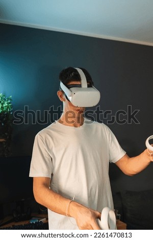 A young guy is wearing virtual reality VR goggles or headset playing in virtual reality in his room during the day