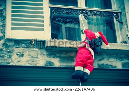 Santa Claus climbing up a wall into a window. Traditional Christmas decoration. Aged photo.