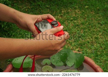 Hand holding red camera while take a picture with leaf object