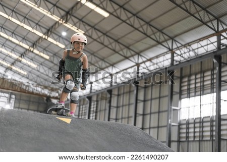 asian child skater or kid girl fun playing skateboard or ride surf skate to start on wave ramp pump track in skate park by extreme sports surfing to wear helmet elbow wrist knee guard for body safety Royalty-Free Stock Photo #2261490207