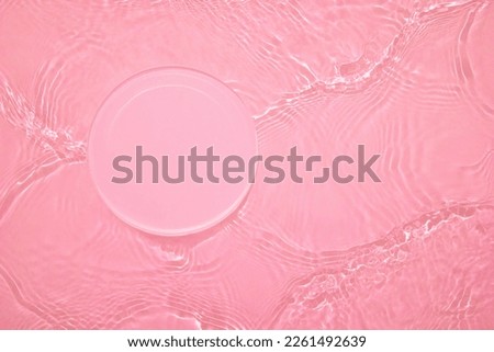 Empty clear glass circle podium on pink transparent calm water texture with waves in sunlight. Abstract nature background for product presentation. Flat lay cosmetic mockup, copy space.
