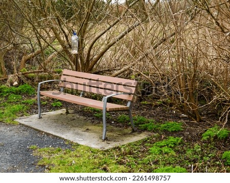Brown plastic bench with metal frame in a park and a home made DIY bird feeder. Scene in a park. Nobody.