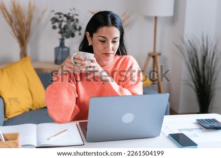 Focused woman working on laptop and drinking coffee