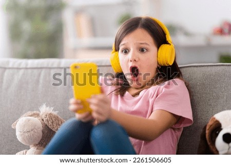 Shocked little girl watching social media content on phone Royalty-Free Stock Photo #2261506605