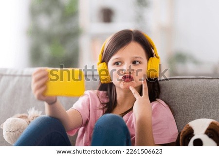 Little girl posing and taking selfie at home, sitting on couch