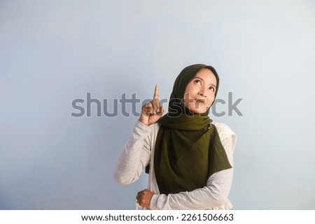 A Portrait of Smiling Asian woman wearing hijab pointing and showing confused expression, empty space.