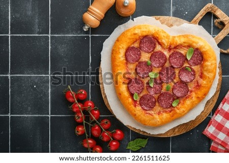 Valentines day heart shaped pizza with mozzarella, pepperoni and basil, wine bottle, two wineglass, gift box on black background. Idea for romantic dinner Valentines day. Top view. Mock up.