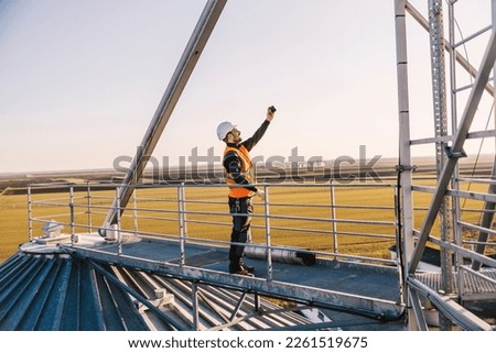 An industry worker is standing on high metal construction and taking selfies.