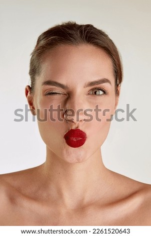 Kisses. Young beautiful brunette girl with red lips posing over grey studio background. Femininity. Concept of natural beauty, skin care, cosmetology, cosmetics, health, fashion, plastic surgery