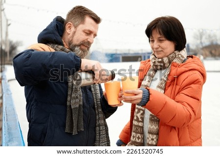 Warming drink. Middle-aged couple, man and woman visiting open air ice rink, drinking tea from thermos. Concept of leisure activity, winter hobby and sport, vacation, fun, relationship, emotions.