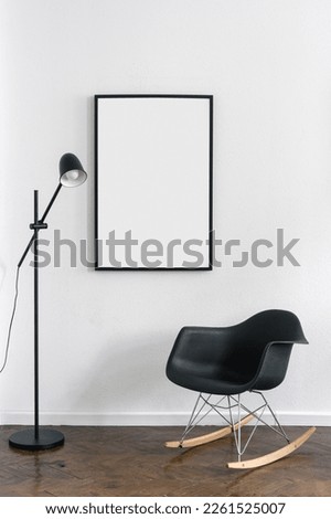 rocking chair, floor lamp and blank picture in black frame hanging on white wall in living room with modern interior, home decoration and furnishing concept