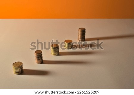 columns with different euro coins in the form of an ascending graph, economic growth on a white and orange background