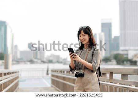 Young Asian woman backpack traveler using mobile phone in express boat pier on Chao Phraya River in Bangkok. Journey trip lifestyle, world travel explorer or Asia summer tourism concept. 