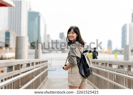 Young Asian woman backpack traveler waiting an express boat at pier on Chao Phraya River in Bangkok. Journey trip lifestyle, world travel explorer or Asia summer tourism concept.  Royalty-Free Stock Photo #2261525421