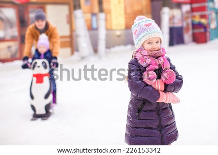 Little girl on skating rink, dad with little sister in the background