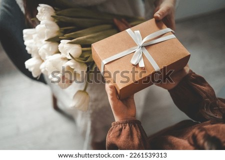 The child's hands hold a beautiful gift box with a ribbon and white tulips. Top view, close-up. Happy mother's day. Royalty-Free Stock Photo #2261539313
