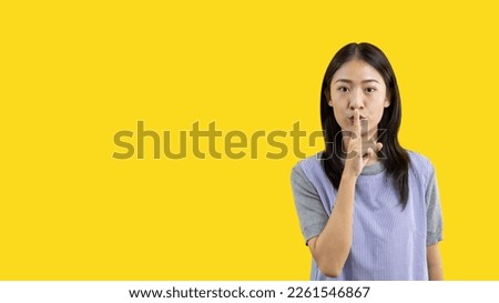 Asian woman doing silent gesture with finger, Noiseless symbol, Noisy mall, Hide a secret, Do not speak. shut your mouth, Noiseless signal transmission, Isolated on yellow background. Royalty-Free Stock Photo #2261546867