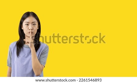 Asian woman doing silent gesture with finger, Noiseless symbol, Noisy mall, Hide a secret, Do not speak. shut your mouth, Noiseless signal transmission, Isolated on yellow background. Royalty-Free Stock Photo #2261546893