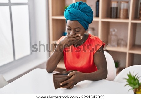 Young african american woman looking empty wallet at home Royalty-Free Stock Photo #2261547833
