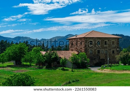 An old brick manor with 3 floors and tiled roof against backdrop of mountains and green grass. Basque Country, Spain Royalty-Free Stock Photo #2261550083