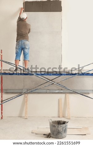 Worker installing tile on wall indoors, back view