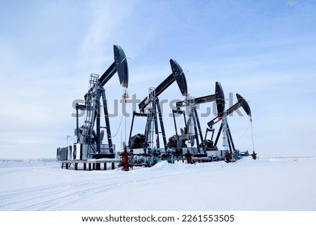 Winter snowy field in prairies and black pump jacks pumping oil.