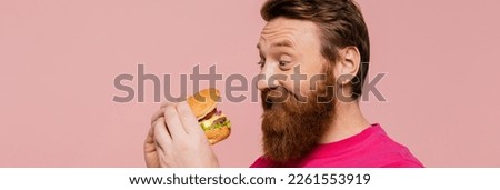 excited bearded man looking at delicious hamburger isolated on pink, banner