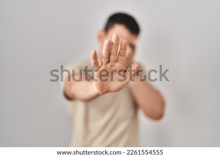 Young arab man wearing casual t shirt covering eyes with hands and doing stop gesture with sad and fear expression. embarrassed and negative concept. 