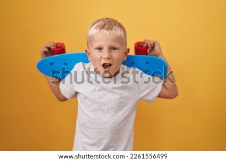 Little caucasian boy holding skate in shock face, looking skeptical and sarcastic, surprised with open mouth 