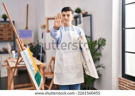 Non binary person at art studio with open hand doing stop sign with serious and confident expression, defense gesture 
