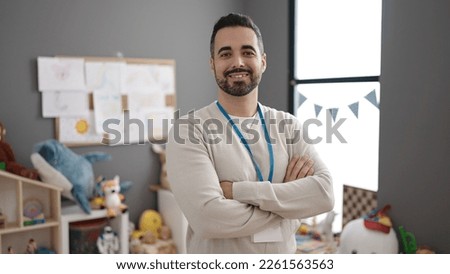 Young hispanic man teacher smiling confident standing with arms crossed gesture at kindergarten Royalty-Free Stock Photo #2261563563