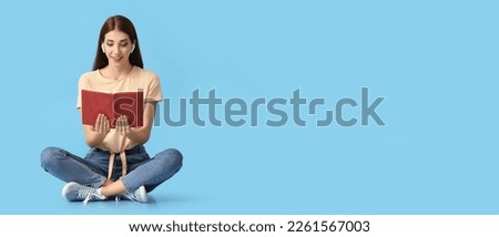 Young woman with earphones reading book on blue background with space for text