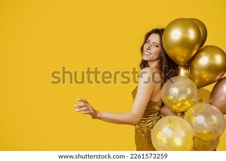 Beautiful lady in dress holding balloons and smiling, being playful on yellow studio background, banner design with blank space. Party time, holiday celebration concept