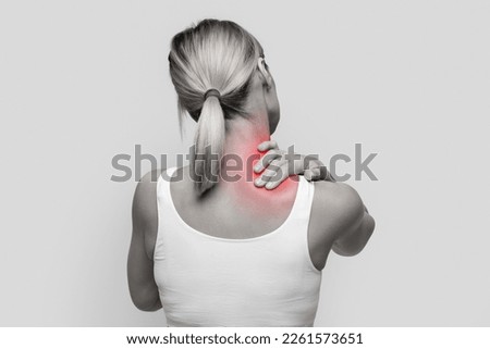 Neck pain muscle stress and strain concept. Stressed blonde woman massaging red sore neck, back view, black and white photo, studio background, copy space Royalty-Free Stock Photo #2261573651