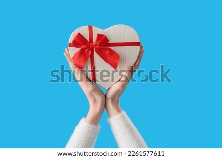 Female hands holding heart-shaped gift on blue background. Valentine's Day celebration