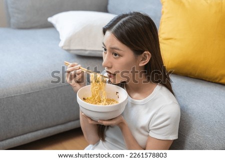 Happy temptation, cute asian young student woman, girl using chopsticks eating instant ramen, noodles soup in bowl while watching TV in living room at home, cooking meal fast food lifestyle of person. Royalty-Free Stock Photo #2261578803