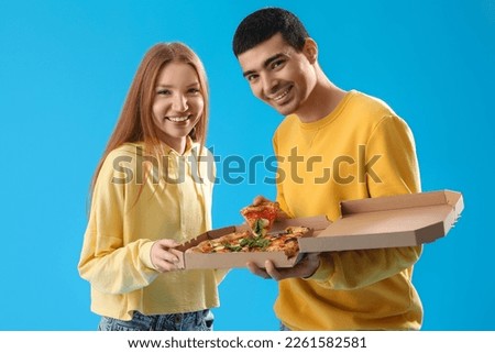 Young couple with box of tasty pizza on blue background Royalty-Free Stock Photo #2261582581
